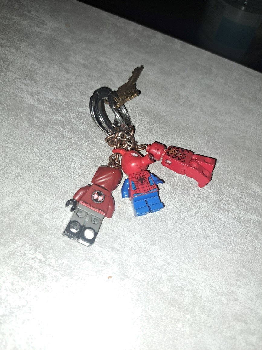 A picture of a key with three lego spiderman keychains attached