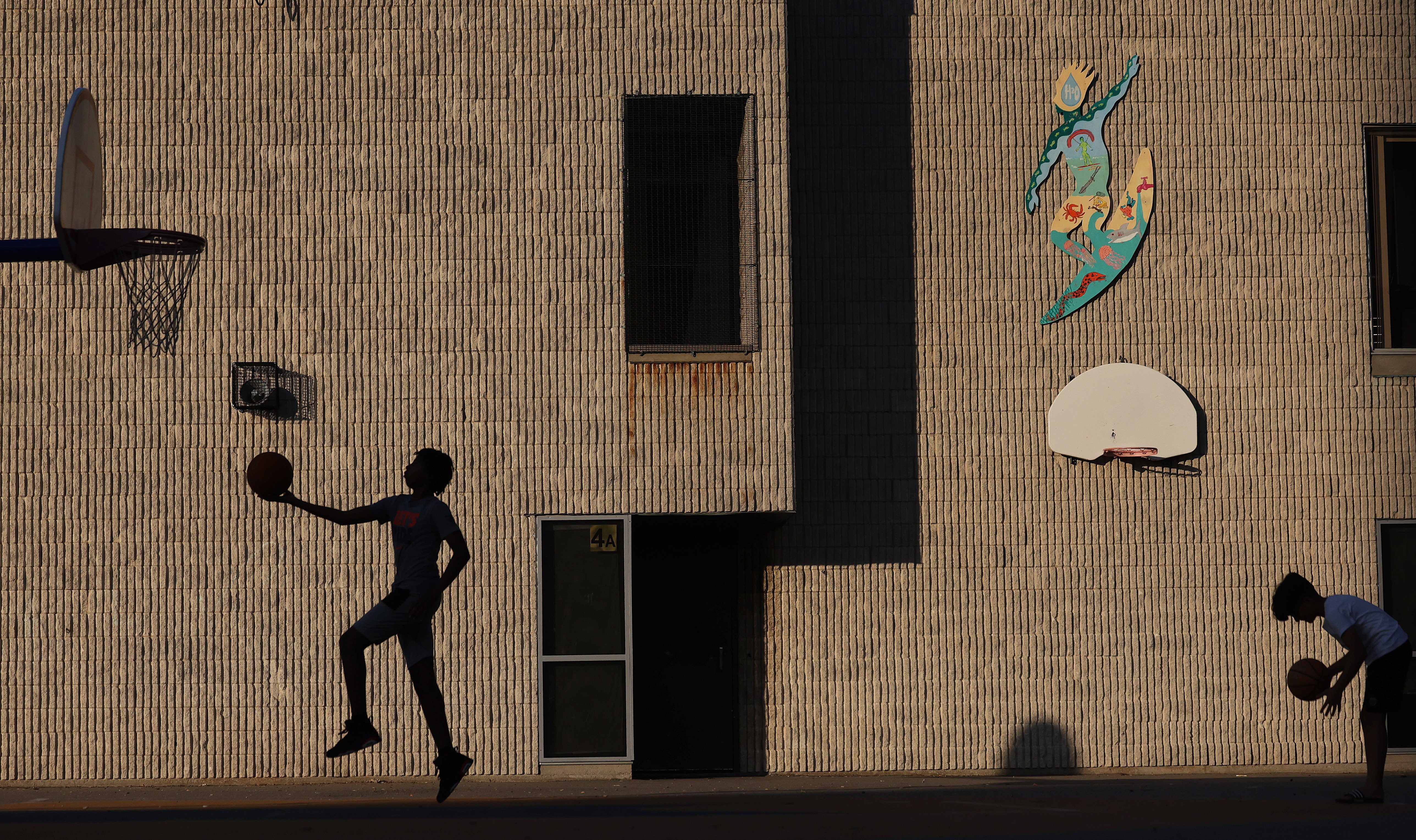 The silhouette of a boy doing a layup in a playground