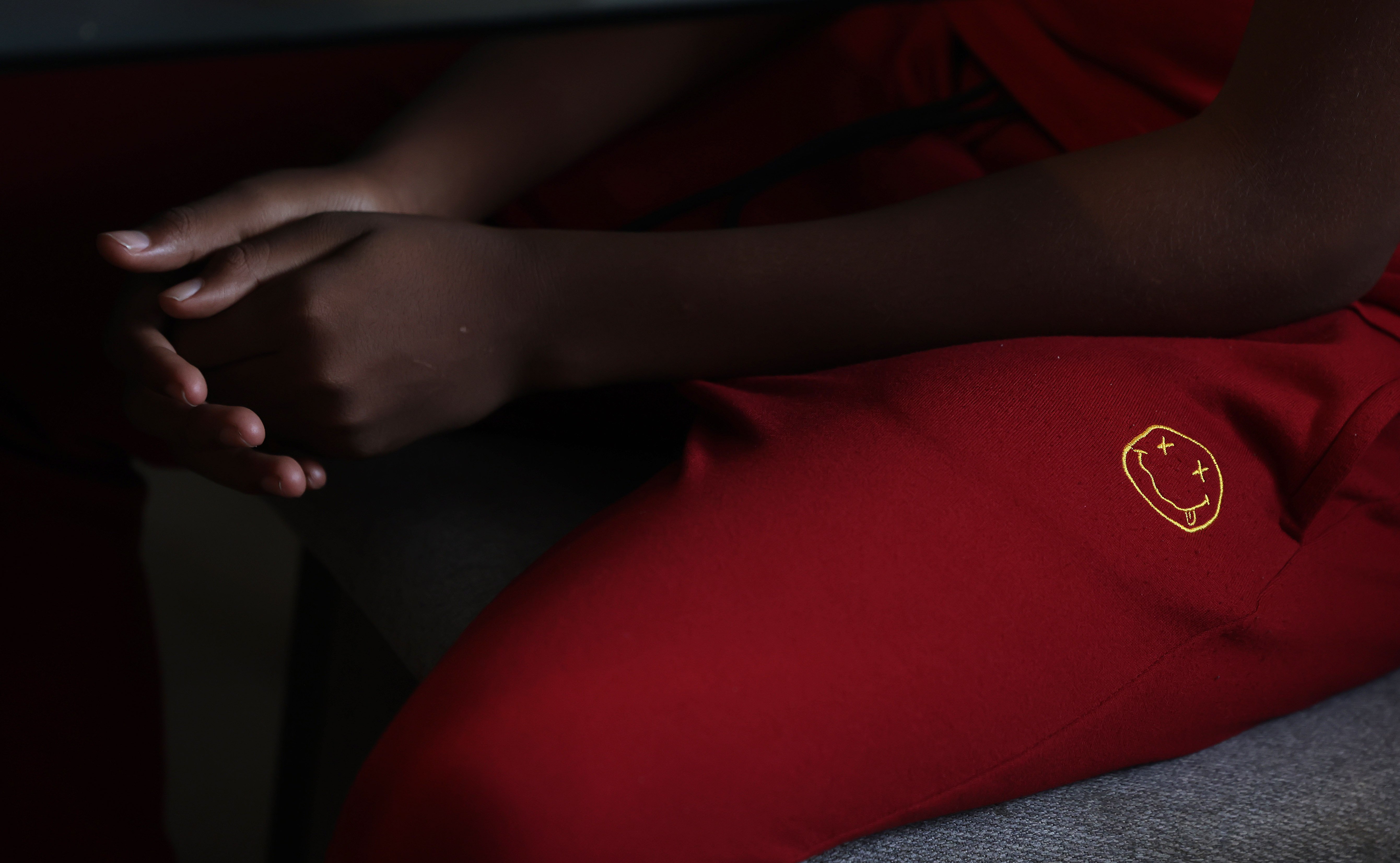 A boys hands resting on his lap. He is wearing red pants
