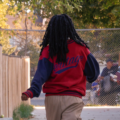 An outdoor photo of a girl with black hair in a red and dark blue bomber jacket
