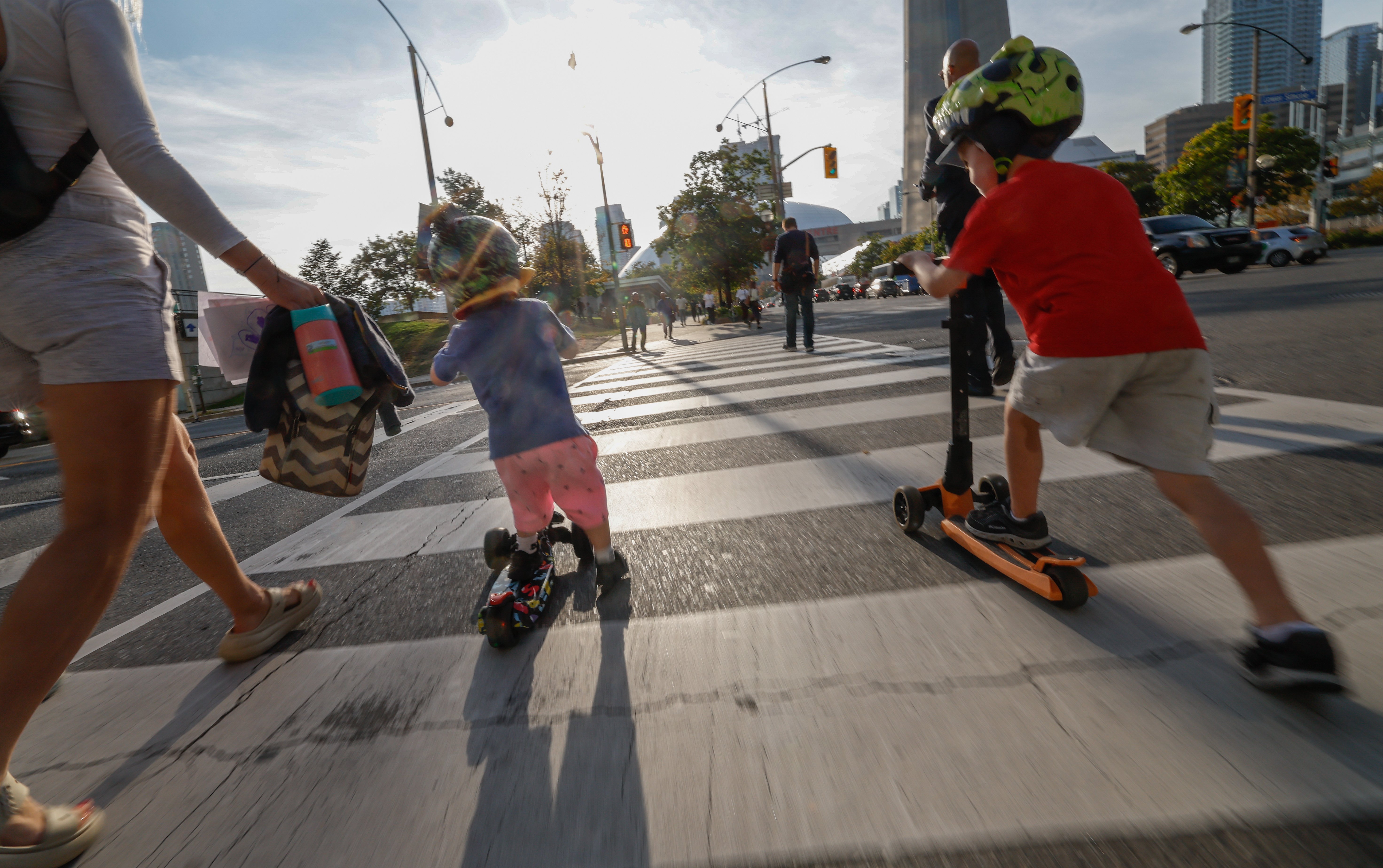 A young boy rides his scooter through a downtown crosswalk.