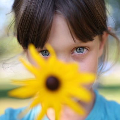 A young girl holds a sunflower in front of her face
