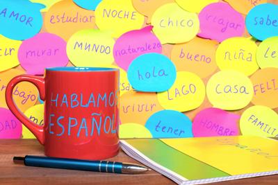 Study Spanish concept, a mug with written words Speak Spanish, notebook, pen and notes with common spanish words.