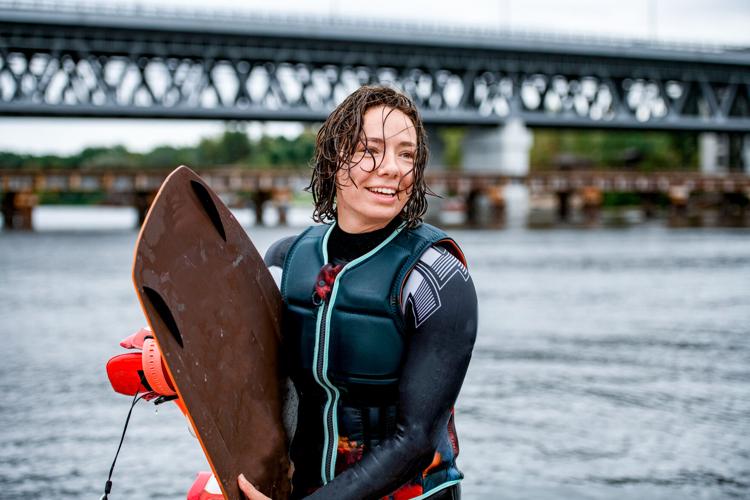 young wet and cheerful woman standing with board for wakeboarding in her hand