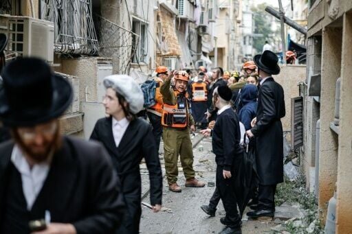A rescuer gestures as Orthodox Jews stand at the scene of an Iranian strike over Bnei Brak in central Israel