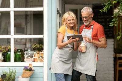 Happy Mature Couple Small Business Owners Using Digital Tablet And Drinking Coffee