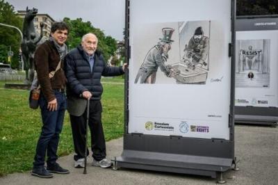 Swiss cartoonist Patrick Chappatte (L) poses with US Nobel prize–winning economist Joseph Stiglitz next to one of his works at the 'Drawings for Freedom' exhibit in Geneva