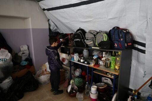A displaced child retrieves his school bag with his books before his online class