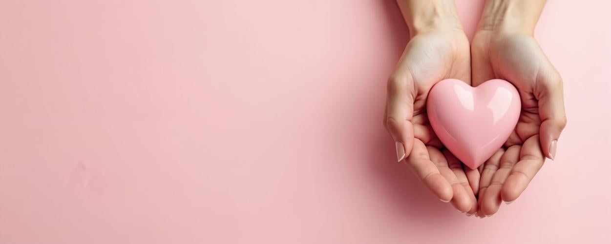 STOCK Female hands gently hold pink heart shape on pastel background. This photo speaks about love compassion tenderness care. Perfect for topics such as valentine romance or wellness.