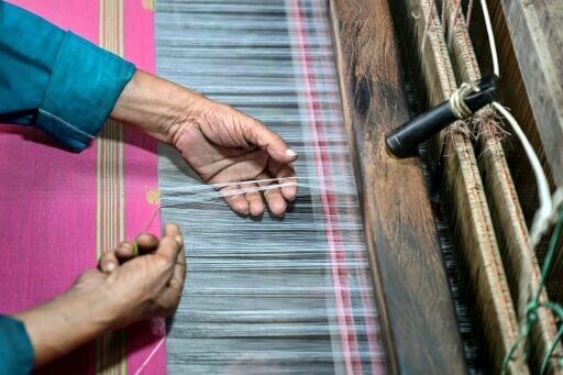 A Bangladeshi craftsman weaves fabric on a traditional handloom inside a workshop in Tangail