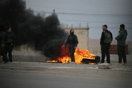 Kurdish fighters stand near burning tires at the entrance to the city of Tabqa in the northern Syrian Raqa province, on January 17, 2026