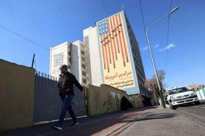 A man walks past a large anti-US mural on the side of a Tehran building