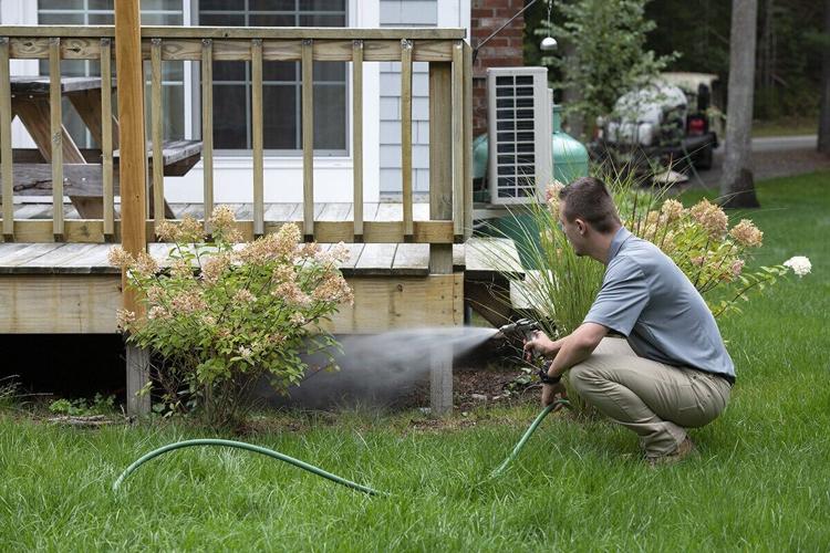 ohDEER technician applying all-natural tick and mosquito control beneath a deck in the backyard of a home.