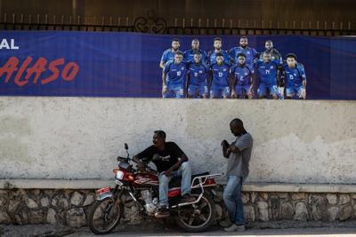 Two men rest in front of a banner of the Haitian national football team in Petion-ville, Port-au-Prince, Haiti, on April 14, 2026.