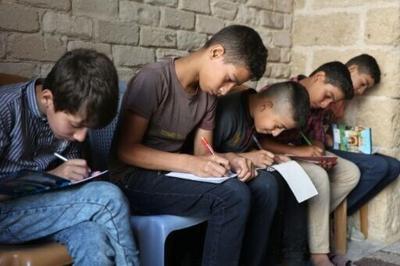 Palestinian children take notes as they attend a class in the historic Al-Kamaliya al-Othmanya school in Gaza City's Old Town, as part of a volunteer initiative organised by displaced teachers, in Gaza City