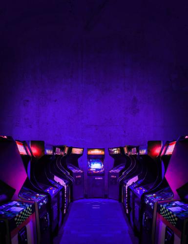 Old Unbranded Vintage Arcade Video Games in dark gaming room with purple light with glowing displays and concrete wall - vertical photo of retro design with free copy space for a poster or magazine