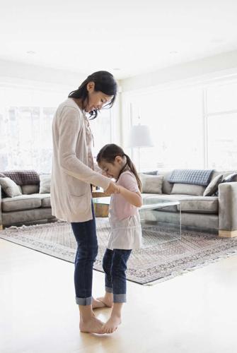 Daughter dancing on mothers feet in living room