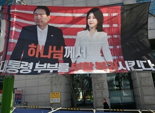 A man walks past a banner showing a picture of South Korea's former impeached president Yoon Suk Yeol and his wife Kim Keon Hee