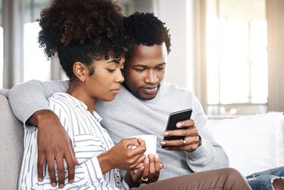 Shot of a young couple using a smart phone together while relaxing on the sofa at home