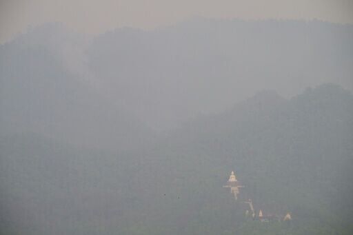 A white Buddha statue shrouded in heavy pollution as smoke rises from a hillside wildfire in Pai, west of Chiang Mai