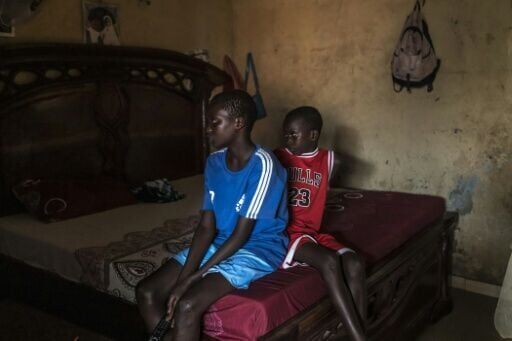 Fallou (L) and Bara (R), who lost their mother in 2024 when her pirogue capsized, watch TV at their home in Mbour, Senegal in March 2026