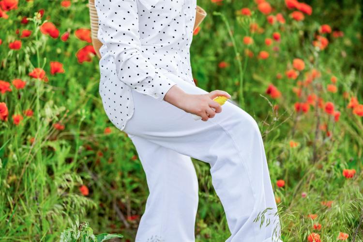 Woman spraying antitick chemical protection on clothes. Safe summer hiking guidelines and body defense against insect bites and lyme disease vectors.
