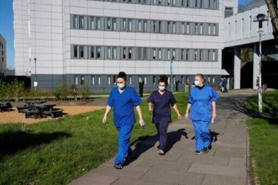 People wearing medical scrubs and face masks walk across campus at the University of Kent in Canterbury which is the centre of a deadly, unprecedented outbreak of meningitis