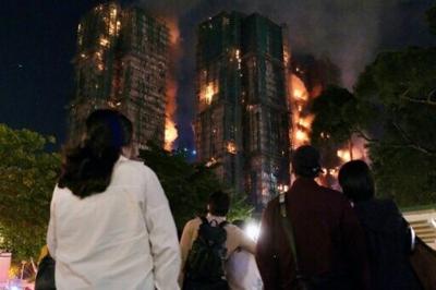 People look on as thick smoke and flames rise during a major fire at the Wang Fuk Court residential estate in Hong Kong's Tai Po district on November 26, 2025