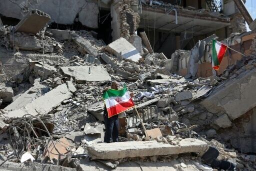 A man holds an Iranian flag amid the debris of a destroyed building following airstrikes in central Tehran on March 4, 2026