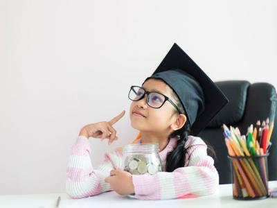 Little Asian girl wearing graduate hat hugging clear glass jar piggy bank and smile with happiness for money saving to wealthness succesful in the future of education concept select focus shallow depth of field with copy space