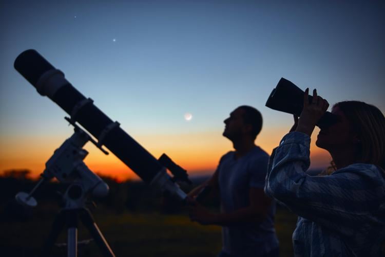 Stock Couple stargazing together with a astronomical telescope.