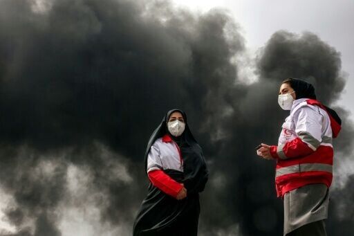 Members of Iran's Red Crescent society stand near smoke caused by an overnight on an oil facility in northwestern Tehran