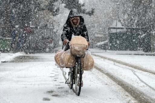 An Afghan man rides a bicycle along a road during snowfall in the green zone area of Kabul on January 22, 2026.