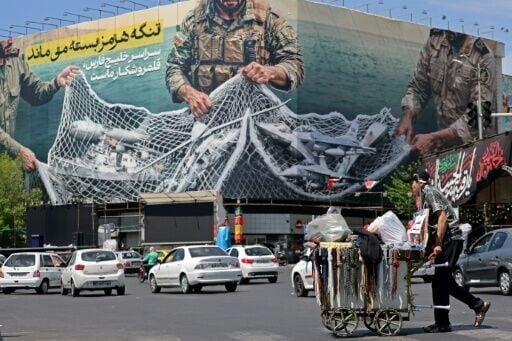 In Tehran, a vendor pushes his cart past a giant billboard reading 'The Strait of Hormuz remains closed'