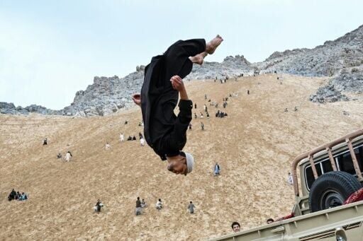 An Afghan parkour athlete performs a stunt on the back of a vehicle in the sandy mountainside at Reg-e-Rawan