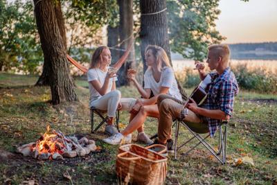 Best friends playing guitar and having fun at bonfire on picnic at the lake