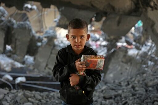 A Palestinian boy holds his belongings amid the debris of a damaged building in Zeitoun