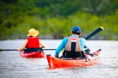 Couple paddling in kayaks on summer day with live vests on