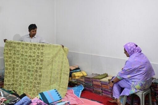 A Bangladeshi shopkeeper shows a traditional Tangail sari to a customer at a store in Tangail