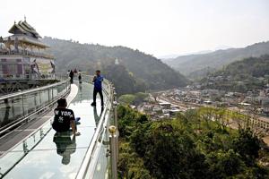 Visitors walk on a skybridge overlooking Myanmar's border town of Tachileik (R) at Wat Phra That Doi Wao Buddhist temple in Mae Sai in the northern Thai province of Chiang Rai on March 17, 2026.