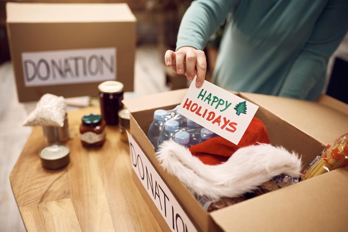 Close-up of woman donating food for charity and adding greeting card with 'Happy Holidays' message into a box.