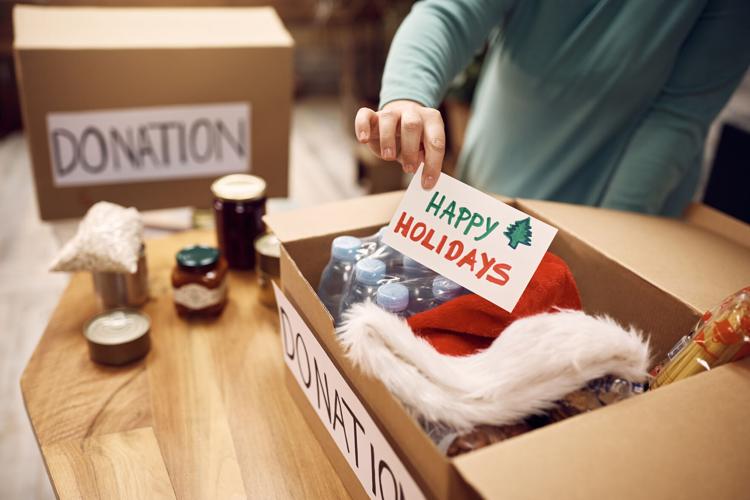 Close-up of woman donating food for charity and adding greeting card with 'Happy Holidays' message into a box.