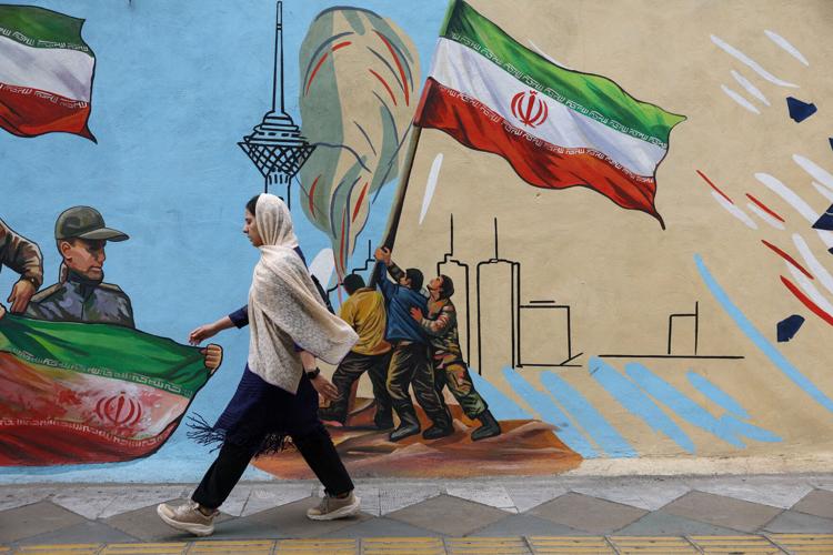 An Iranian woman walks next to a mural on a street in Tehran