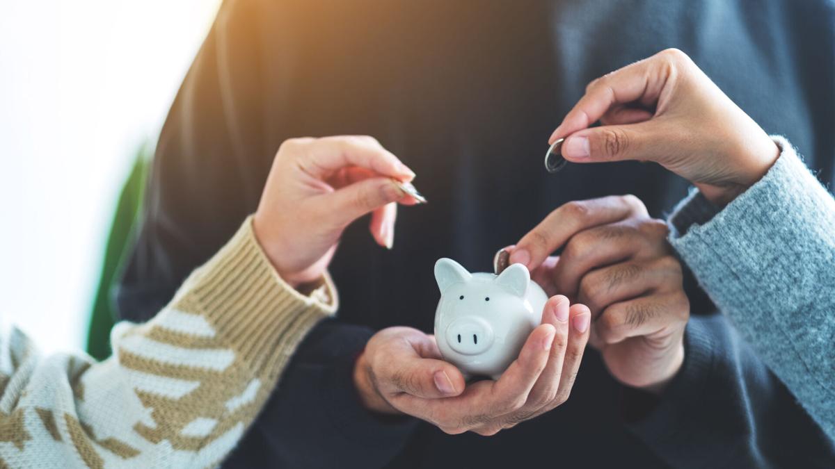 Closeup image of people holding and putting coin into piggy bank
