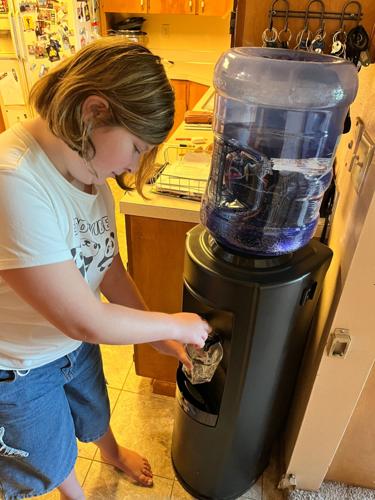Phoebe Hyatt, 11, fills a glass from a water dispenser in her family's kitchen in East Selah, Wash., near the Army's Yakima Training Center. Even after the Army installed a PFAS filter in 2025, the family still drinks bottled water out of an abundance of c