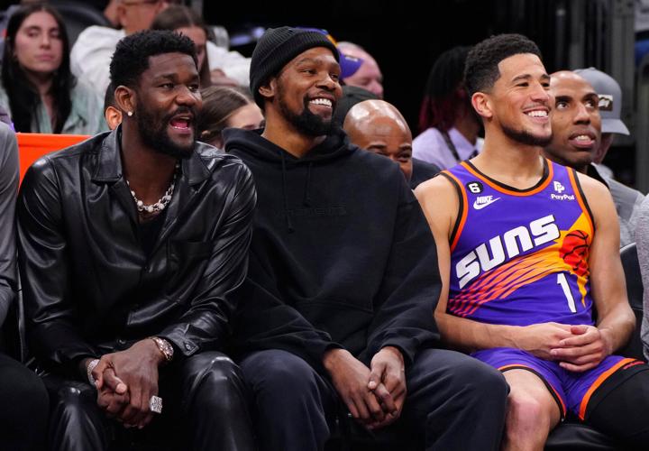 Left to right, Suns Deandre Ayton, Kevin Durant and Devin Booker smile on the bench against the 76ers during a game at Footprint Center in Phoenix on March 25, 2023.