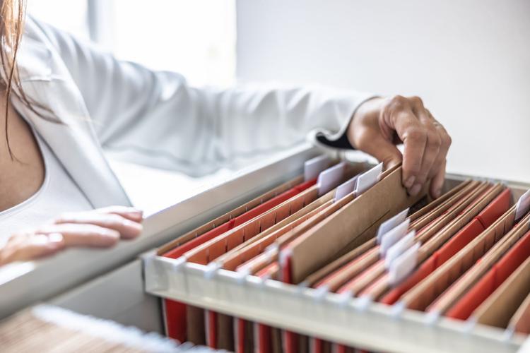 The clerk is leafing through stored folders, looking for a file or document. Concept of data storage, filing cabinet and business administration.