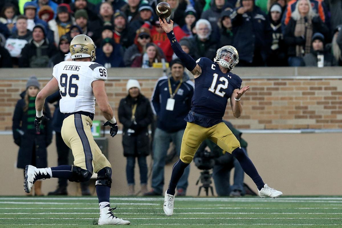 Ian Book (12) of the Notre Dame Fighting Irish throws a pass while being chased by Jackson Perkins (96) of the Navy Midshipmen in the third quarter at Notre Dame Stadium on November 16, 2019 in South Bend, Indiana.