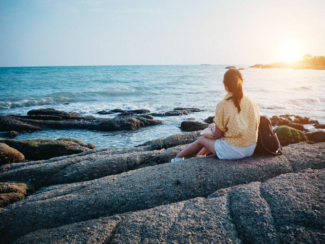 Woman looking to the sea and sitting on the rock. Hipster woman travel at the beach.