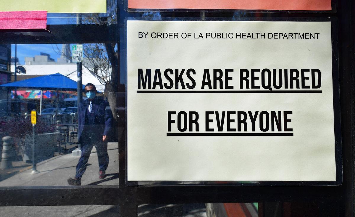 A man wearing a protective face mask walks past a sign requiring face masks posted on a storefront in Los Angeles, California, on March 2, 2022.